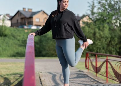 Young woman in activewear stretching on a red railing outdoors.