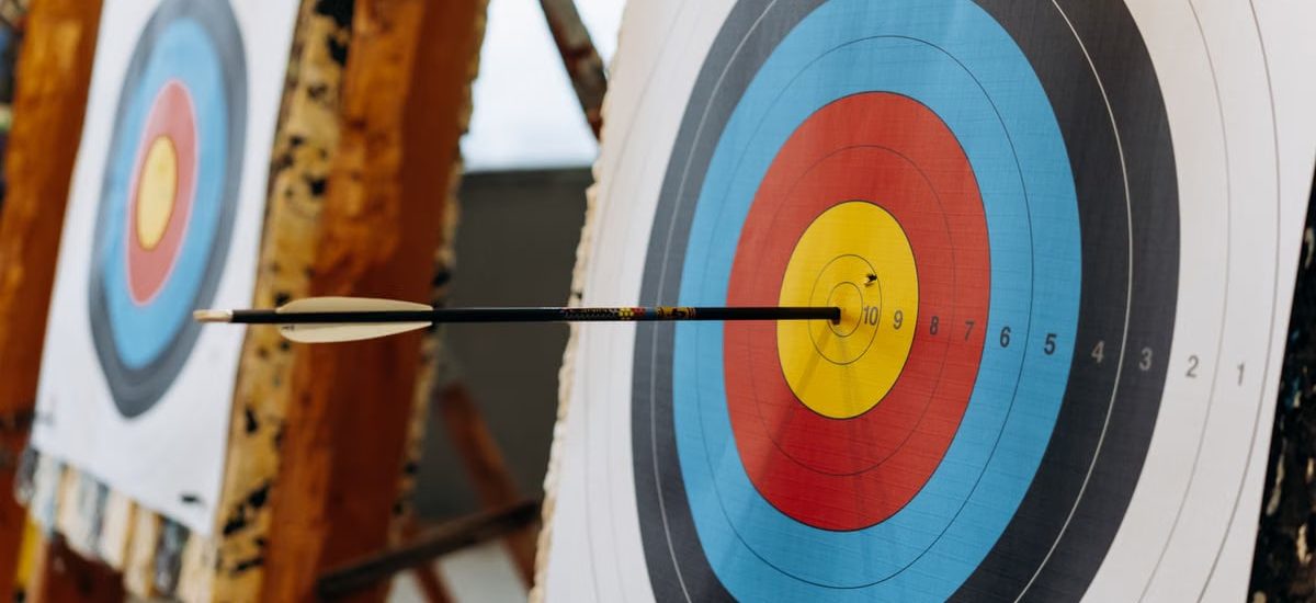 An arrow hits the bullseye on a colorful target in an indoor archery range.