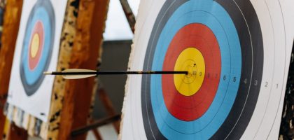 An arrow hits the bullseye on a colorful target in an indoor archery range.