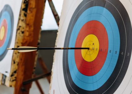 An arrow hits the bullseye on a colorful target in an indoor archery range.